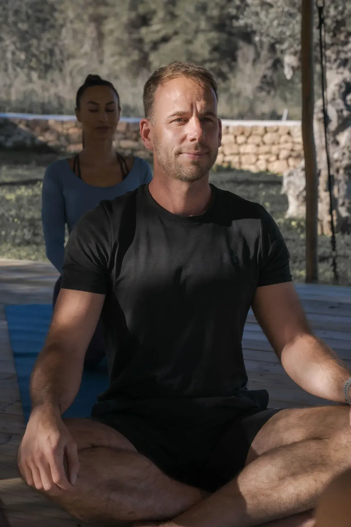 Neil sitting cross-legged in meditation on an outdoor deck